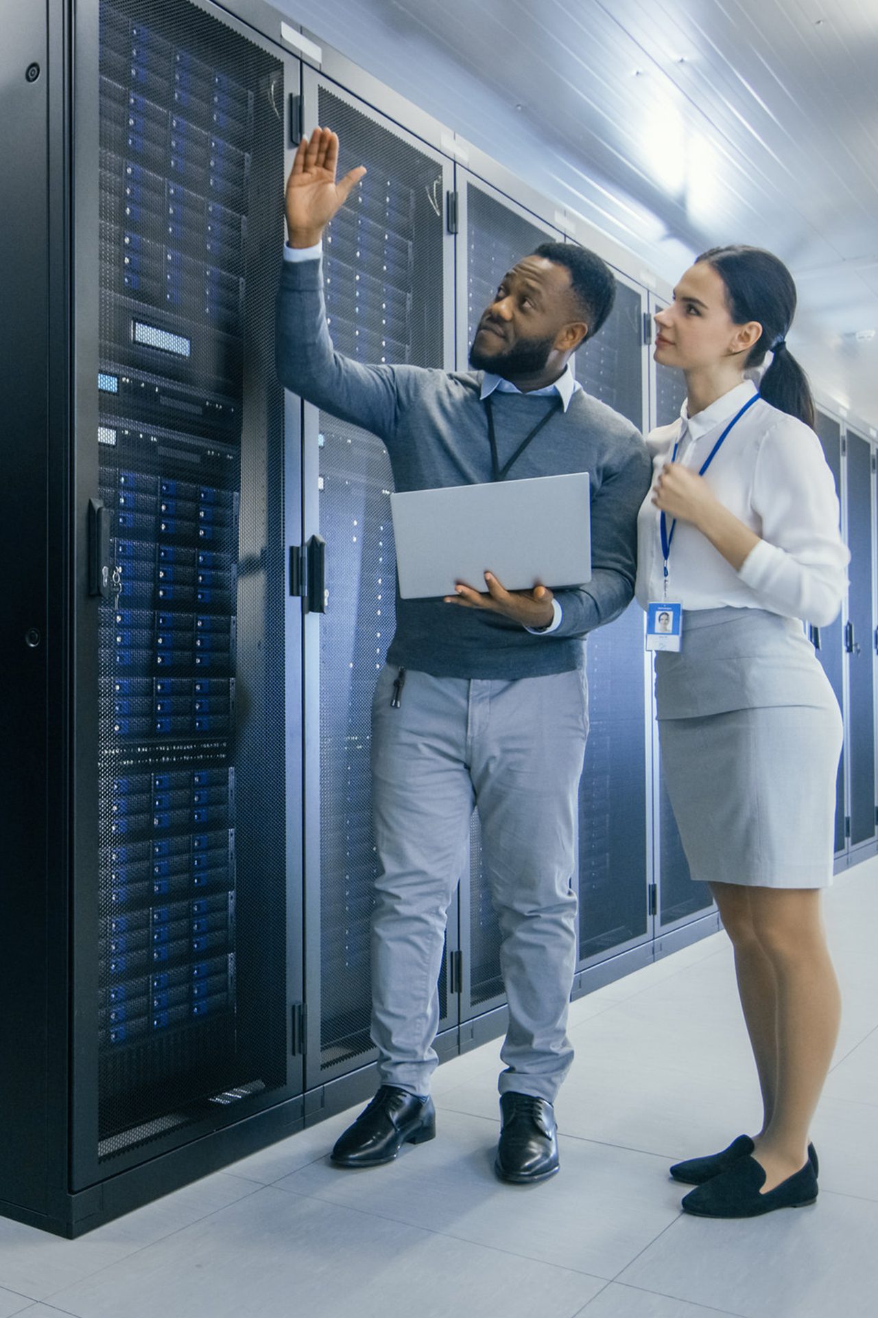 Black IT Technician with a Laptop Computer Gives a Tour to a Young Intern